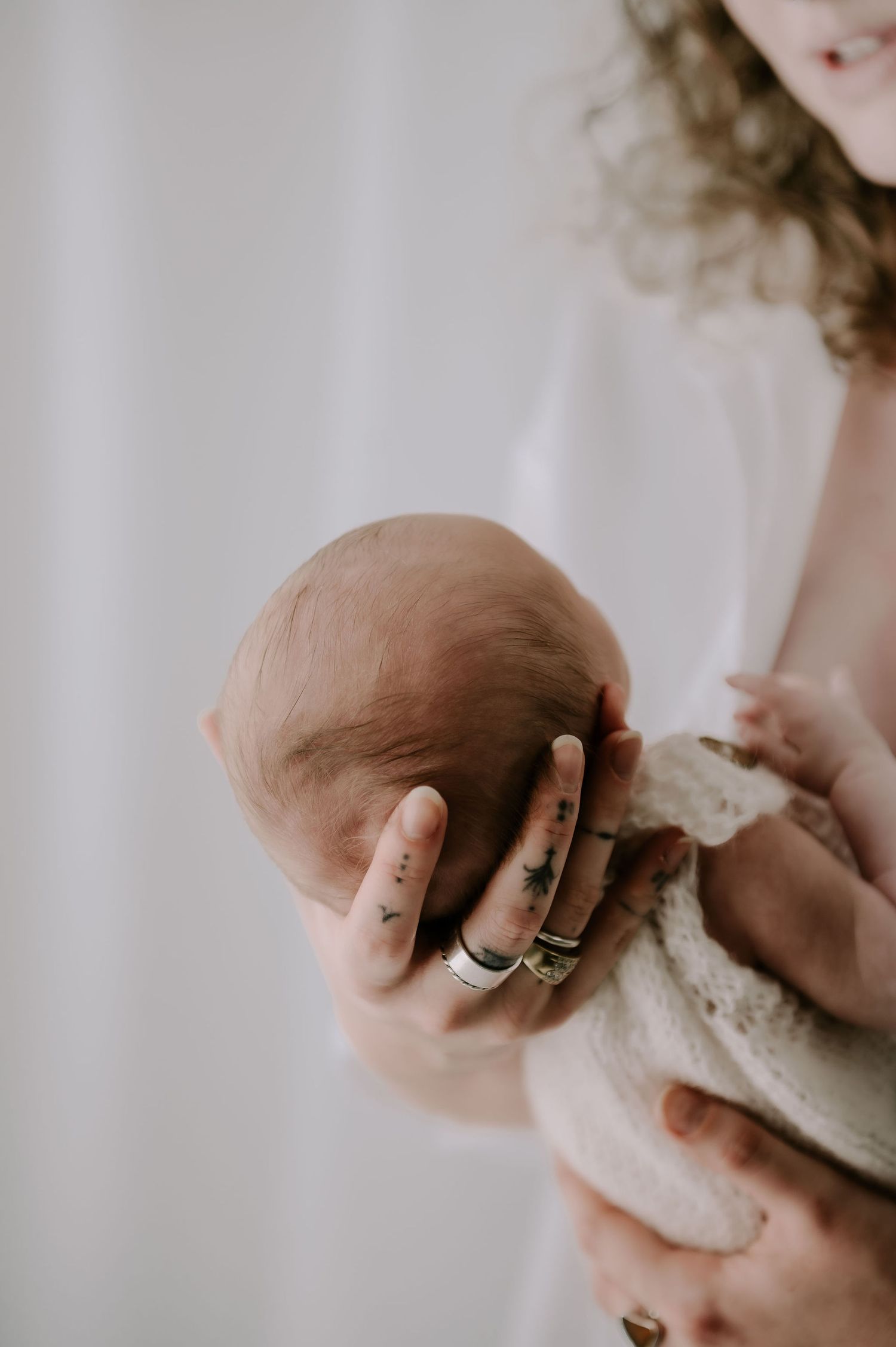 Newborn baby resting in mother’s arms, head gently cradled in her hands, photographed in a studio – Melton Mowbray newborn photoshoot.
