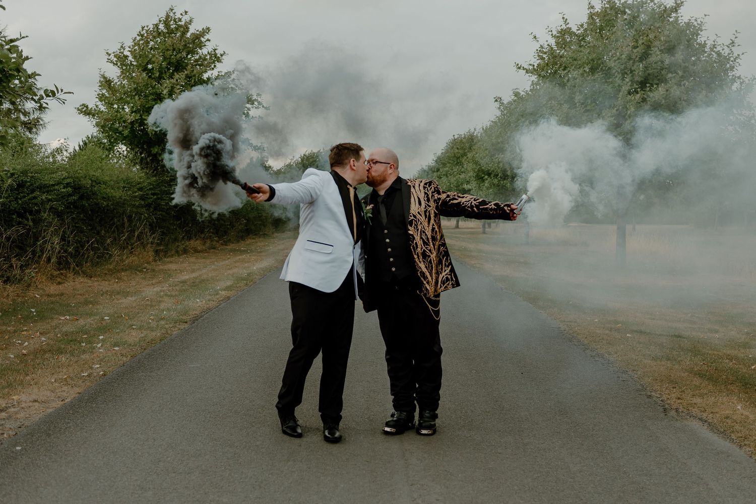 A couple creates moody photo effects with colored smoke bombs on a rural road.