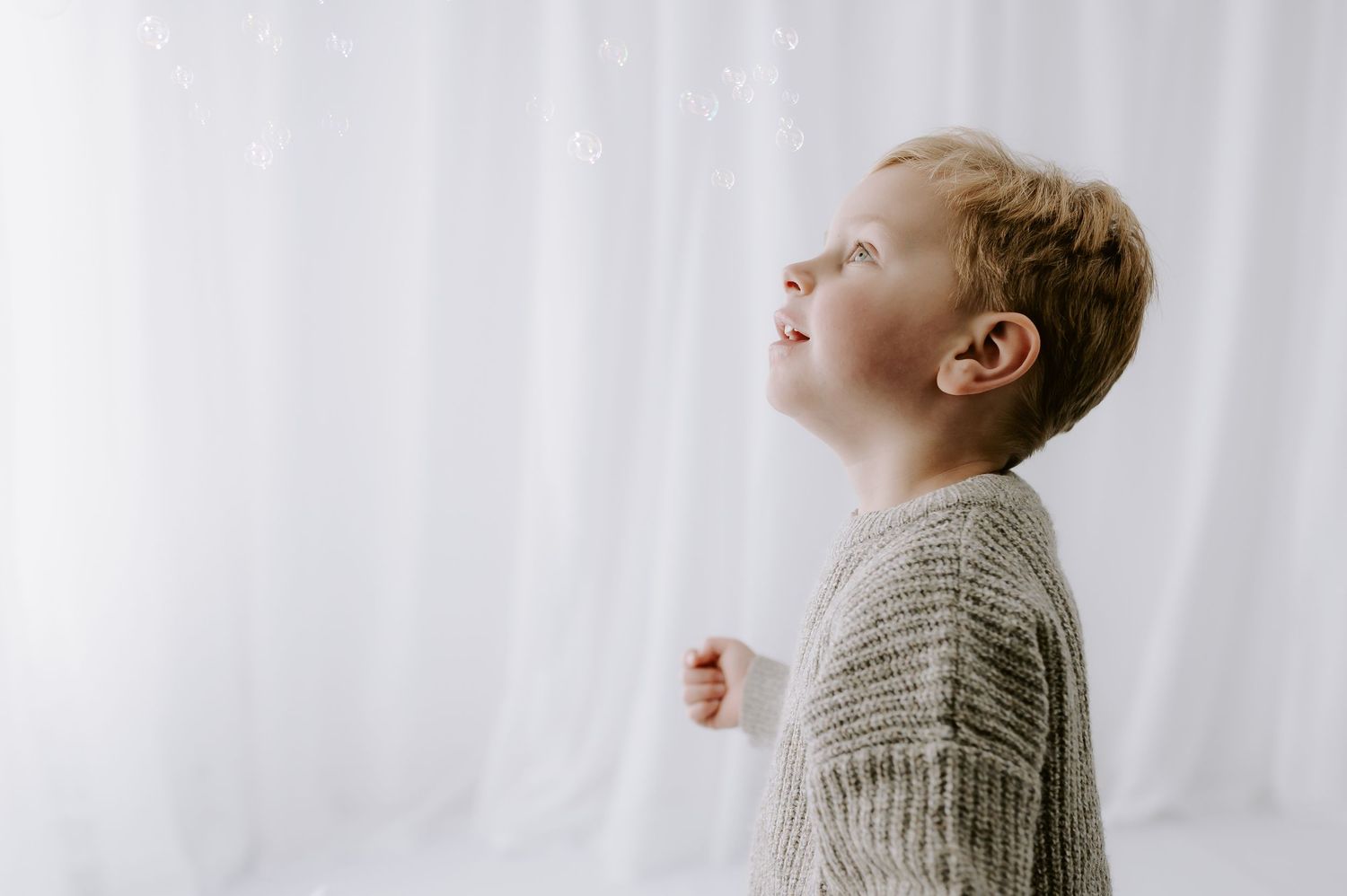 Person in knit sweater looking up smiling, bubbles in air, studio, Melton Mowbray.