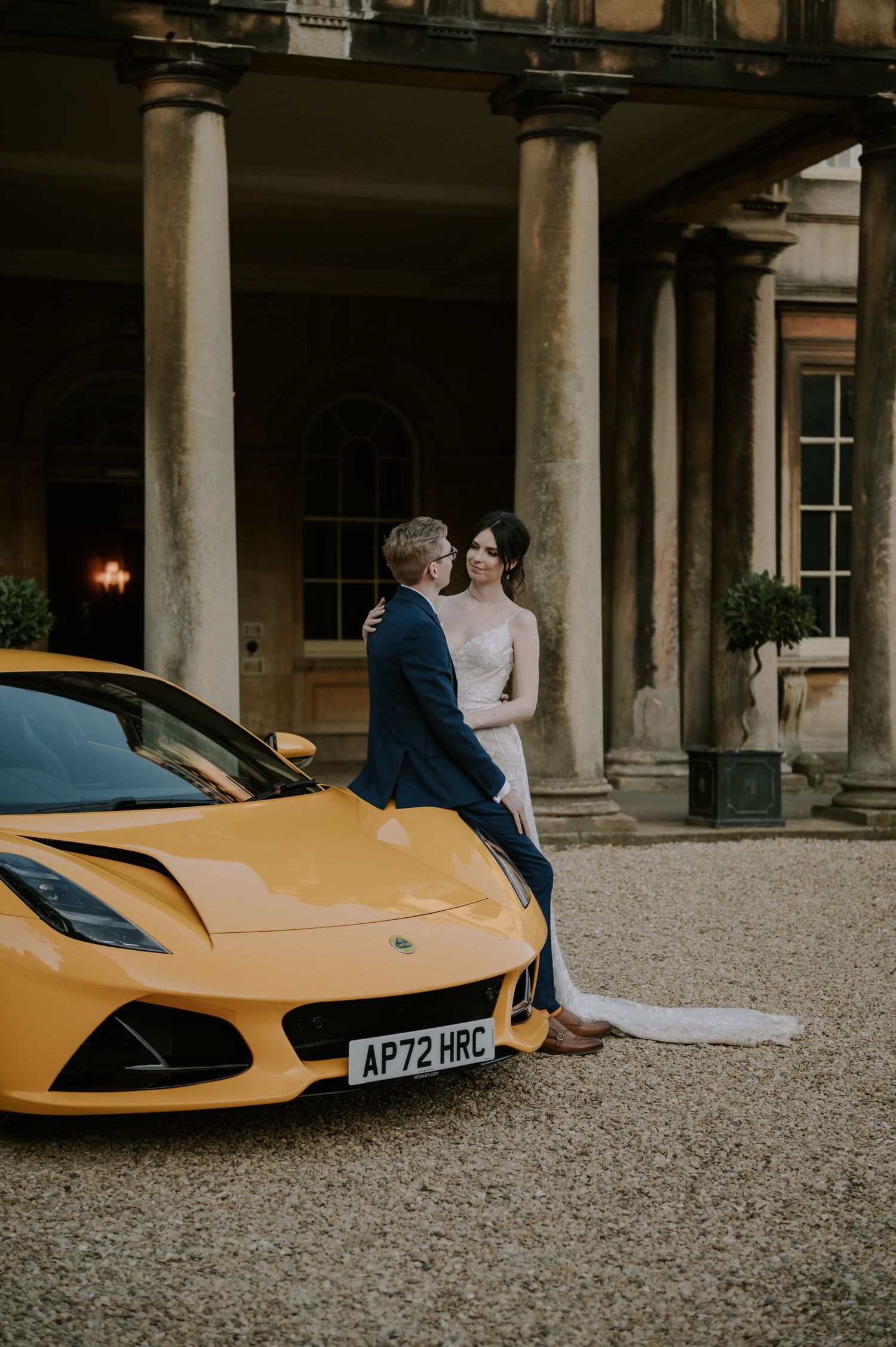 A yellow McLaren sports car parked outside a historic columned building with gravel grounds.