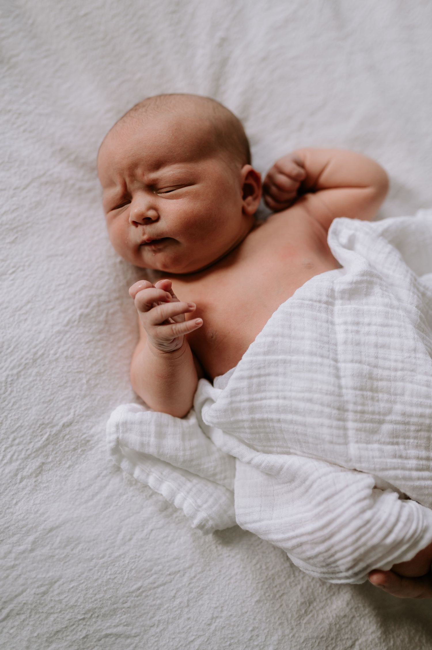 Sleeping newborn in white clothing on soft white textured surface, studio, Melton Mowbray.