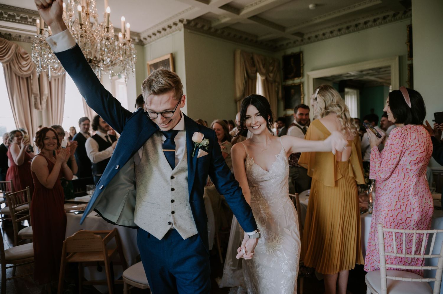 Wedding guests dance together during a joyful celebration in an elegant venue decorated with chandeliers.