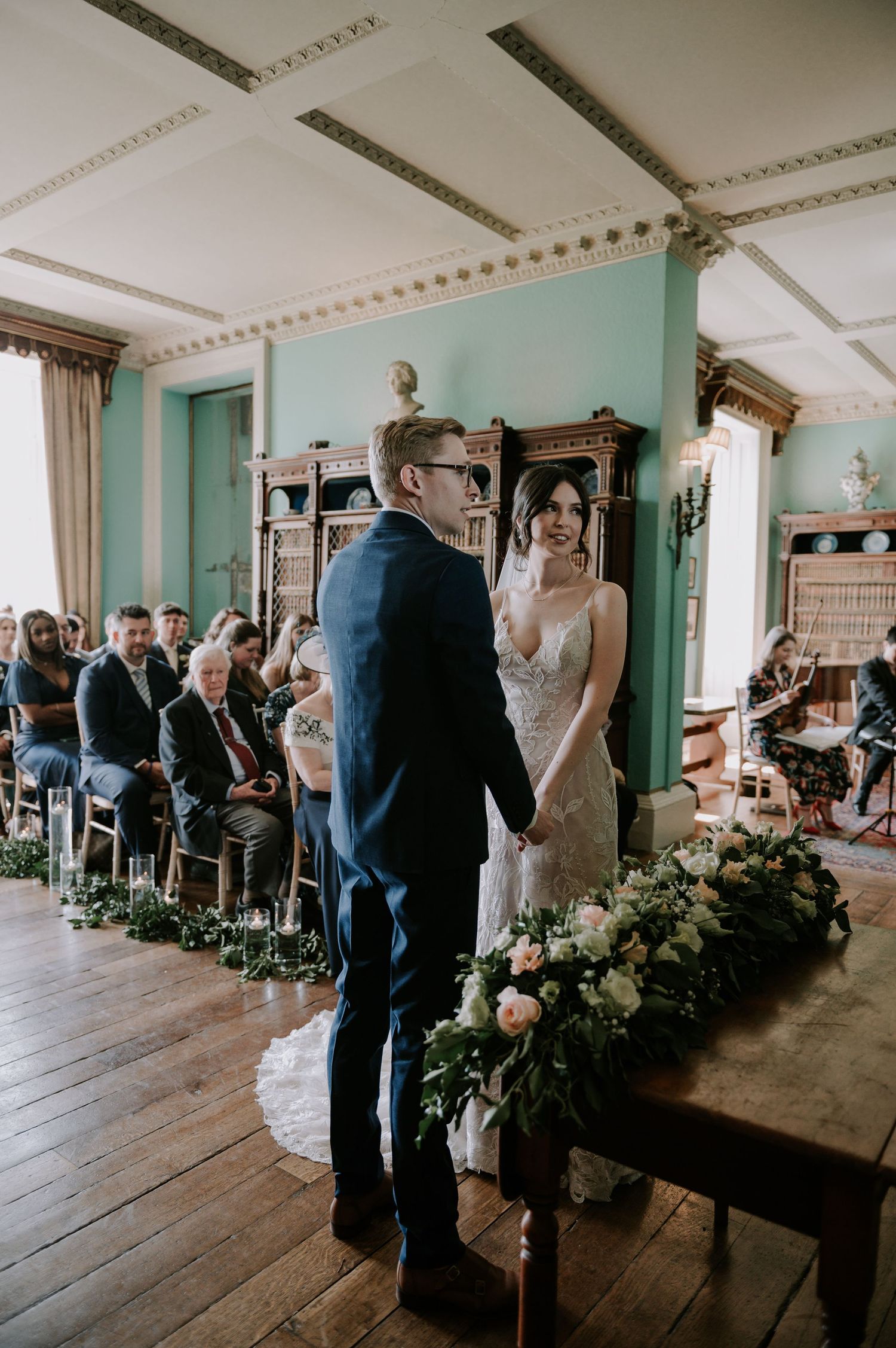 A wedding ceremony unfolds in an elegant room with mint green walls and wooden floors during an intimate gathering.