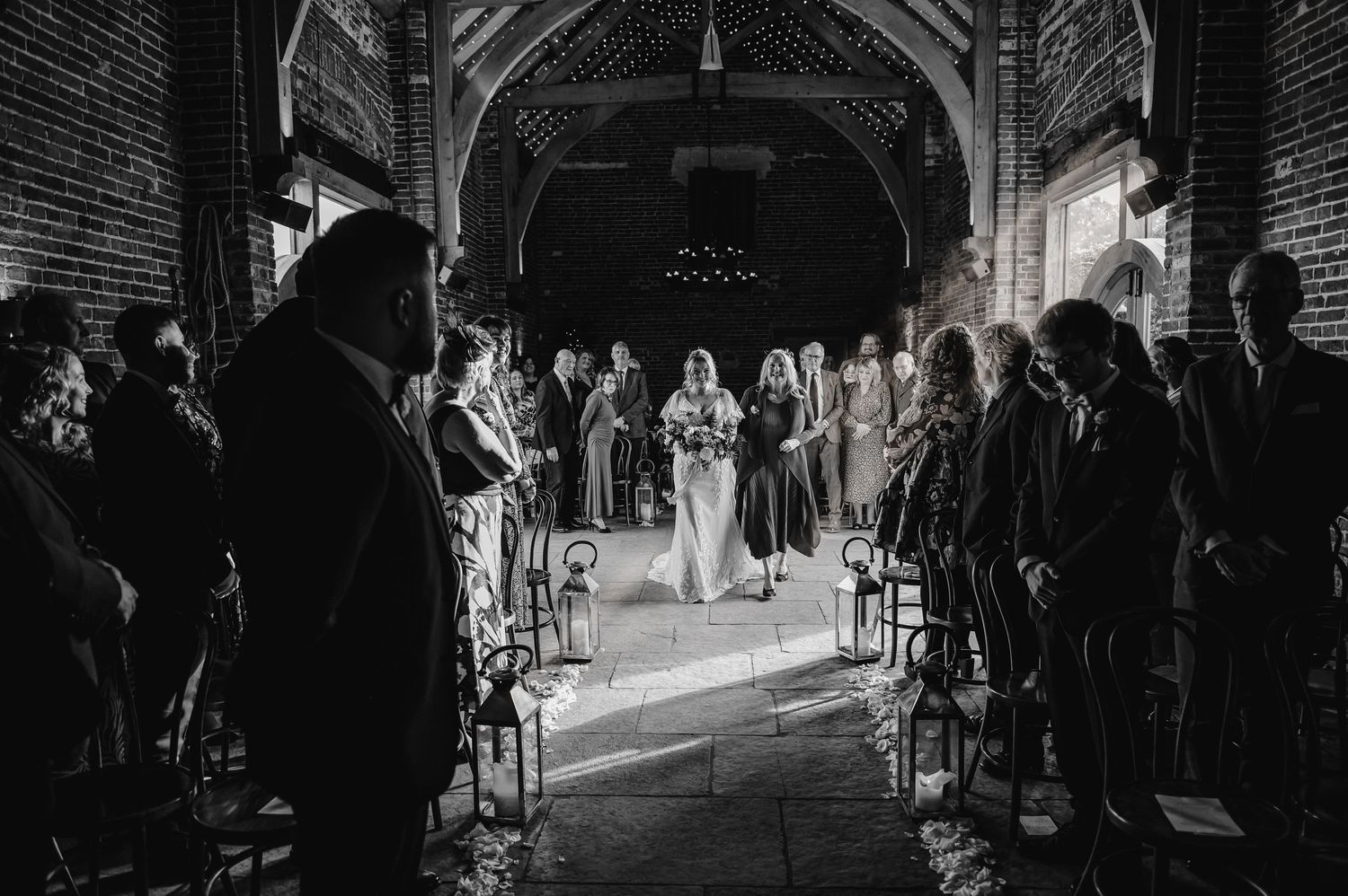 A dramatic black and white wedding ceremony inside a brick chapel with light streaming down the center aisle.
