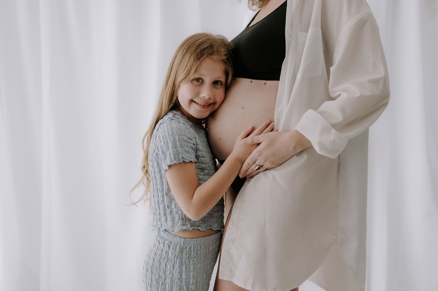 Woman in white dress cradling pregnant belly, girl touching stomach, studio, Melton Mowbray.