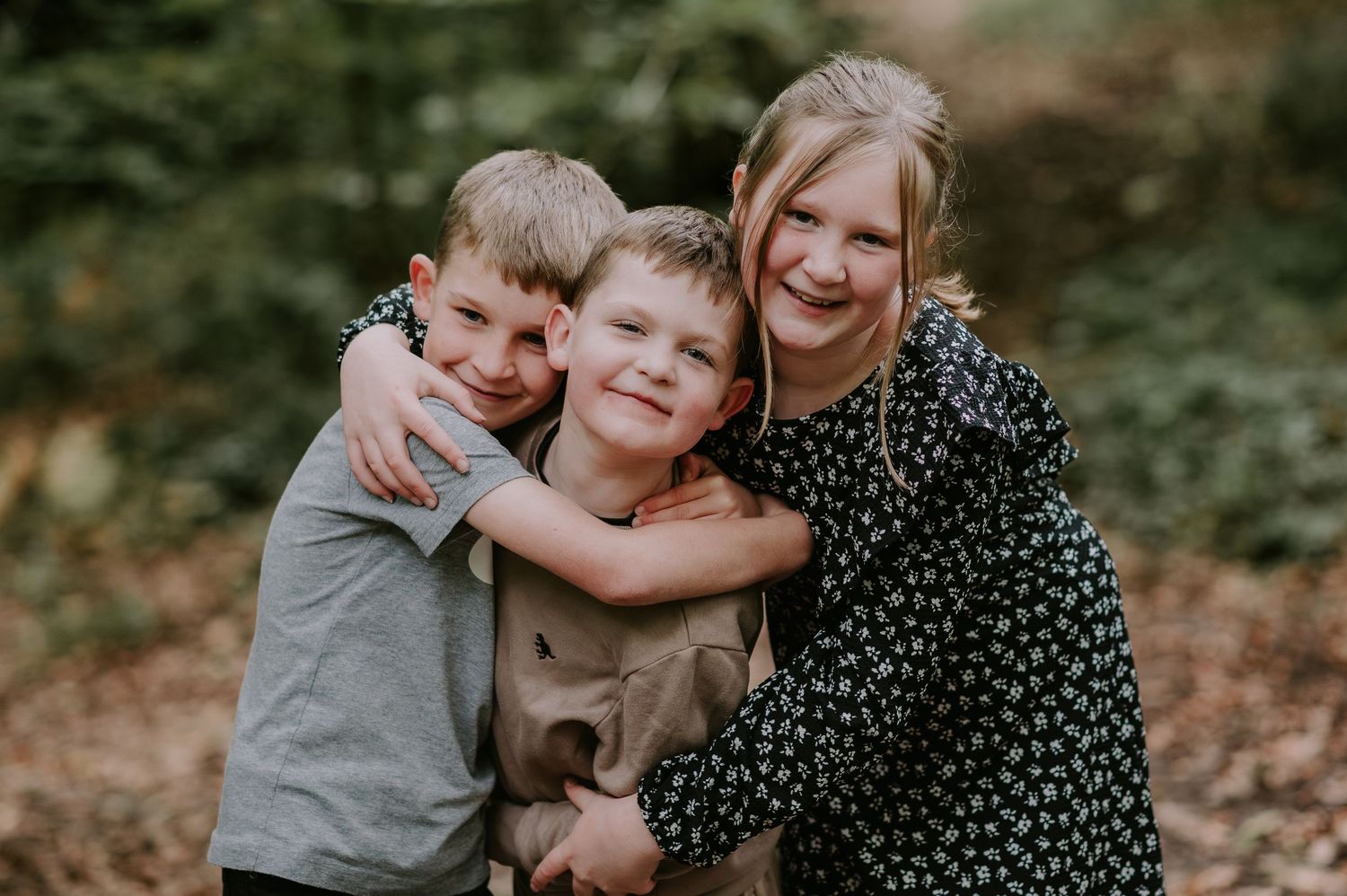 Three young children share a joyful embrace while posing outdoors in a natural setting.