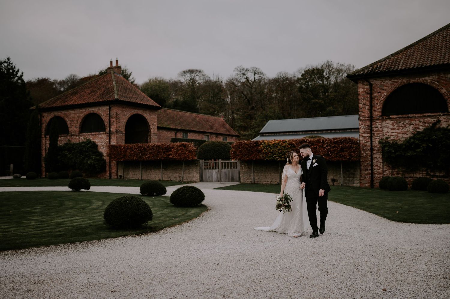 A panoramic view of a rustic brick venue with multiple outdoor spaces lined with trees and white gravel paths.