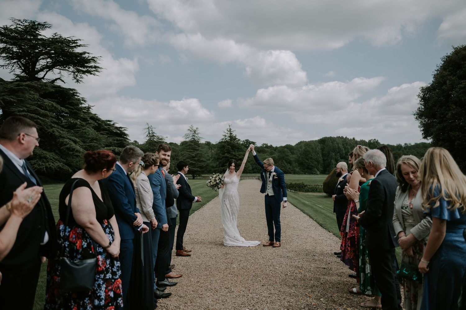 A sequence of wedding guests mingling and conversing outdoors on a path surrounded by greenery.