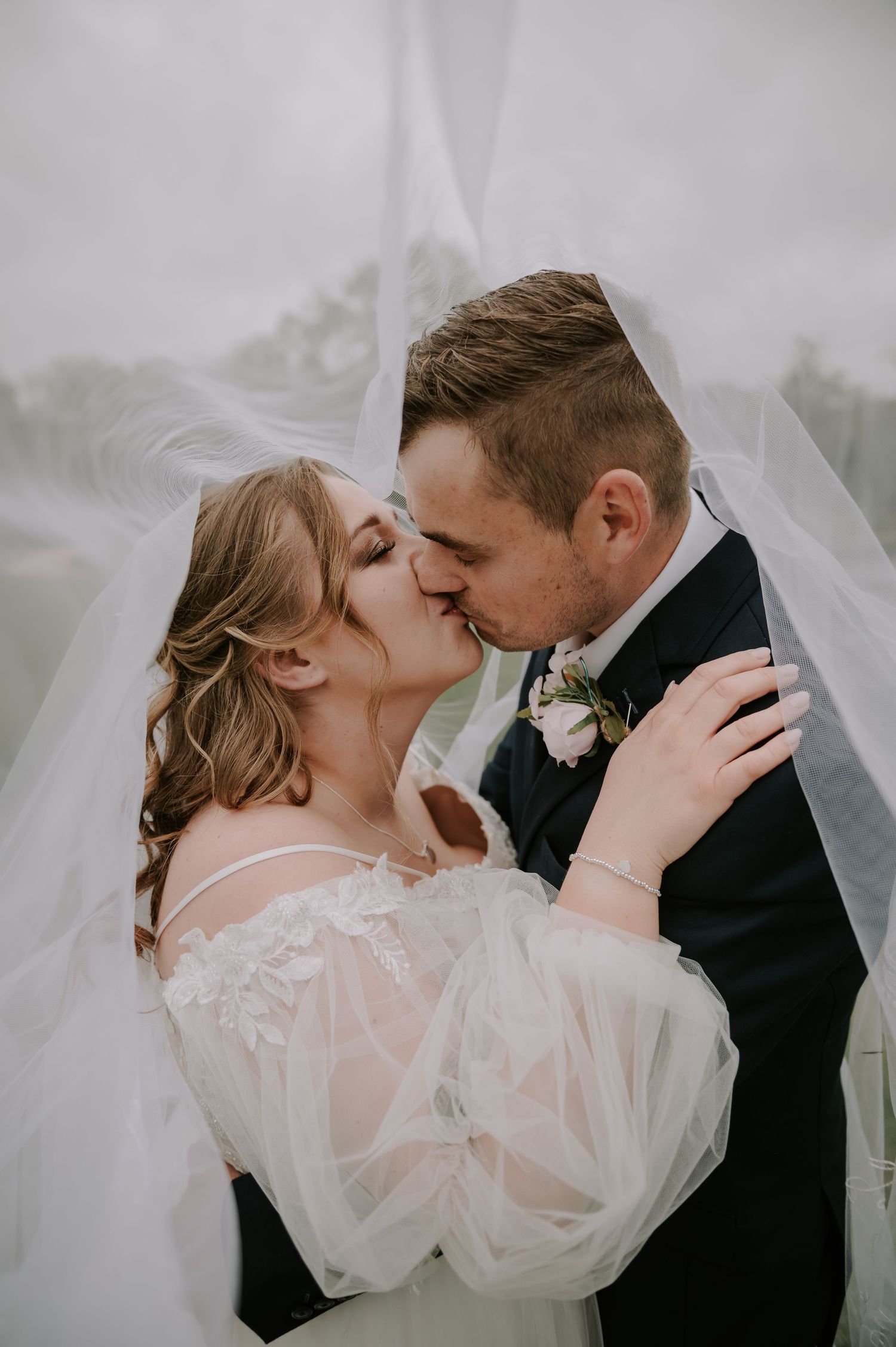 Romantic wedding scene of a couple kissing under sheer white veil with soft dreamy light.