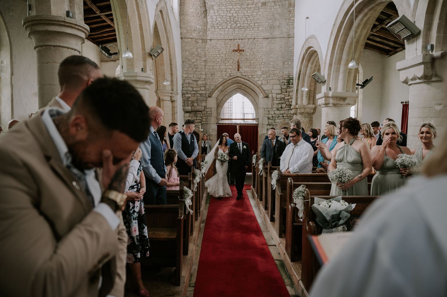 Bride walking down aisle with father, groom waiting, hands covering eyes, Melton Mowbray wedding.