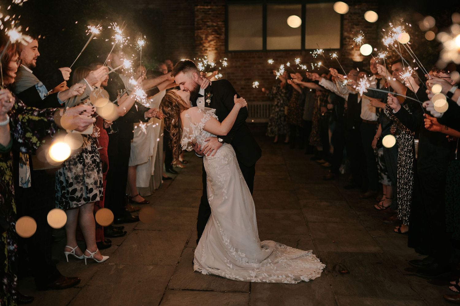 Newlywed couple sharing romantic kiss during nighttime sparkler exit at wedding reception – Hazel Gap Barn, Derby wedding.