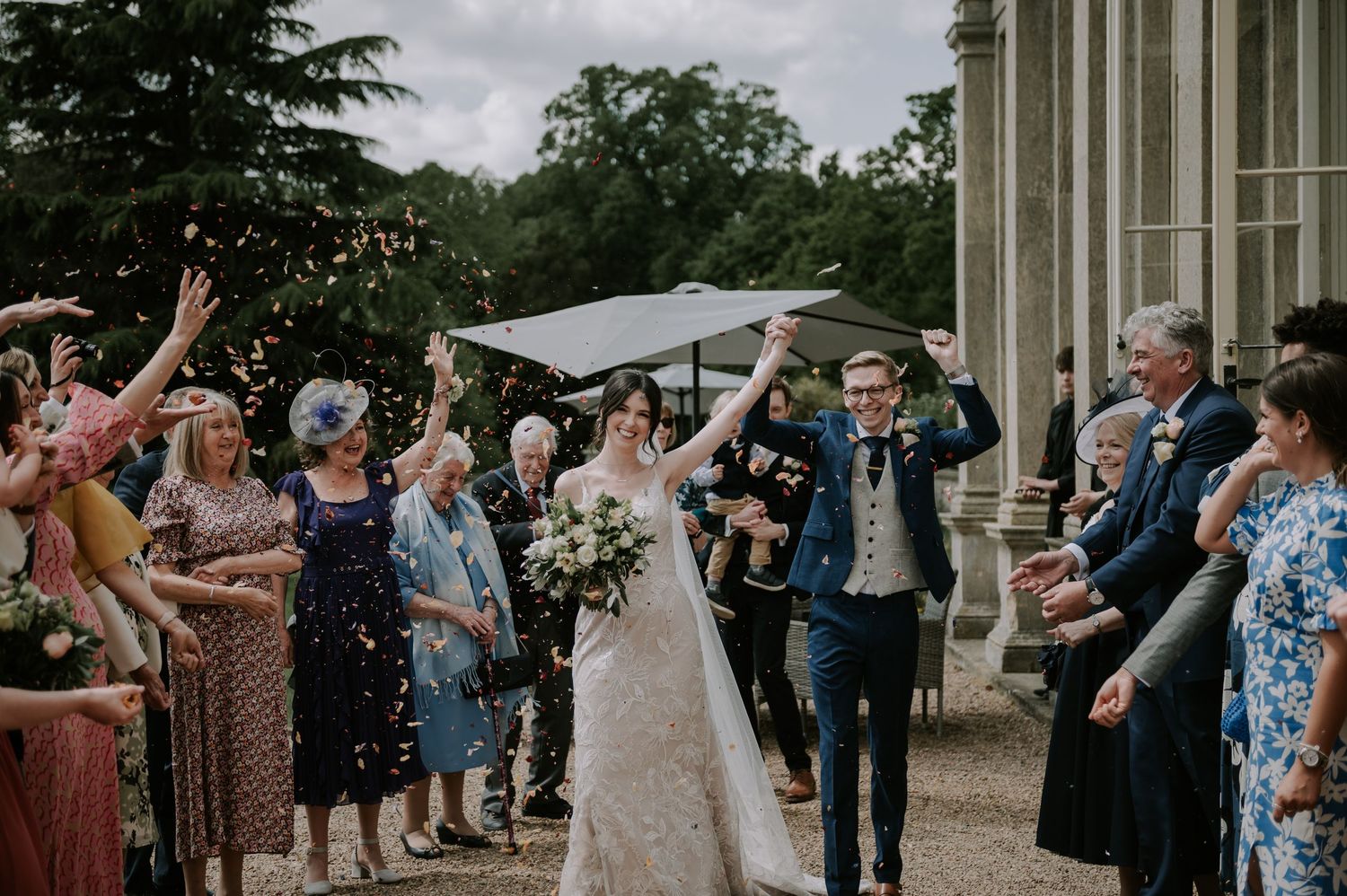 Wedding guests shower the newlyweds with confetti outside a grand columned building during a joyful celebration.