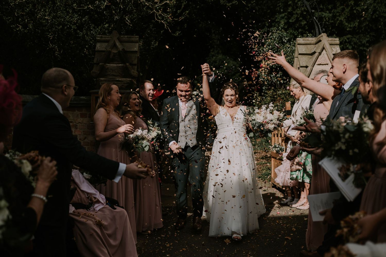 Wedding guests throw confetti during a joyful outdoor celebration as newlyweds walk through the shower of petals.