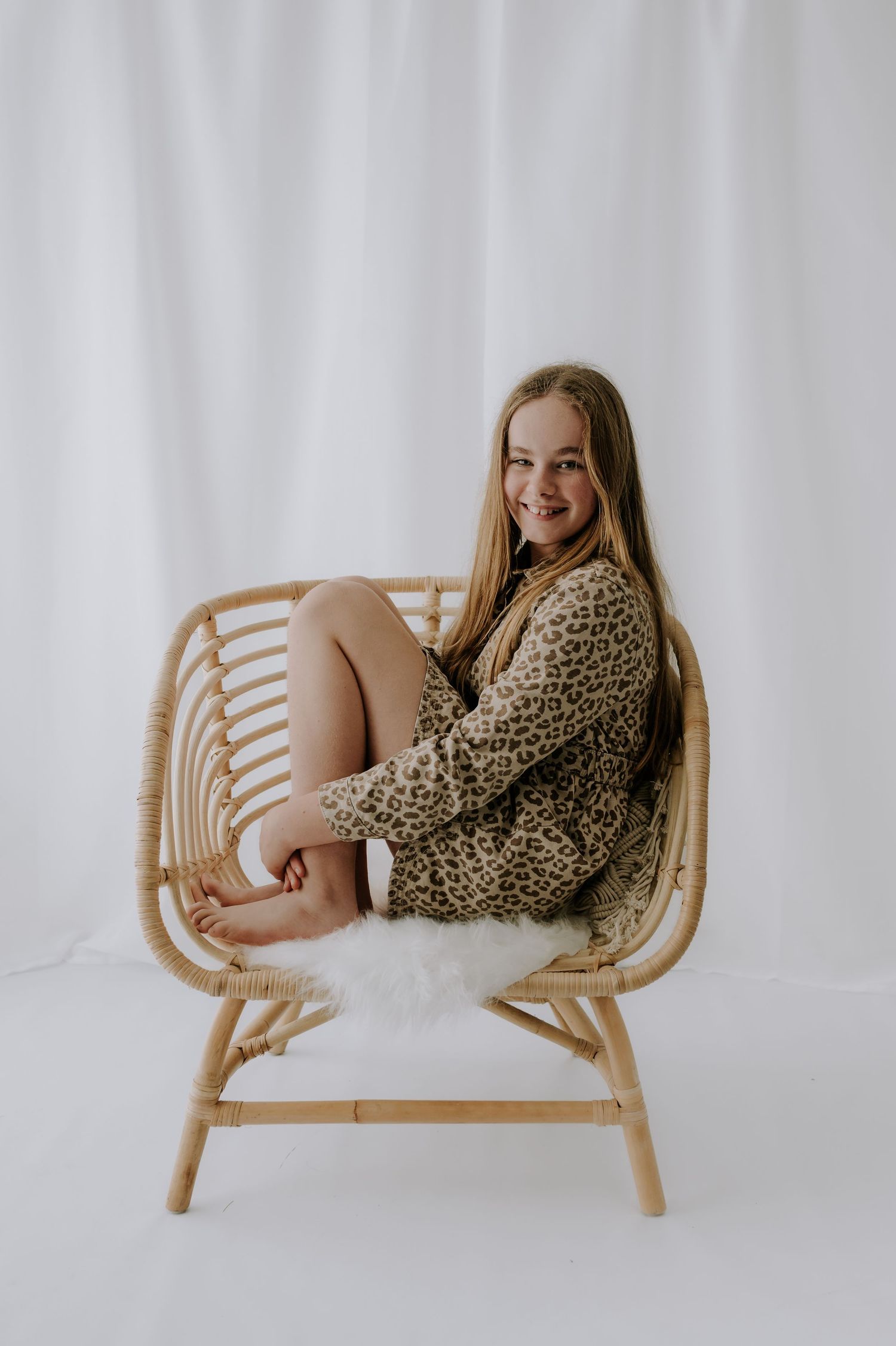 Person in leopard print sweater curled in rattan chair with white fur, studio, Melton Mowbray.