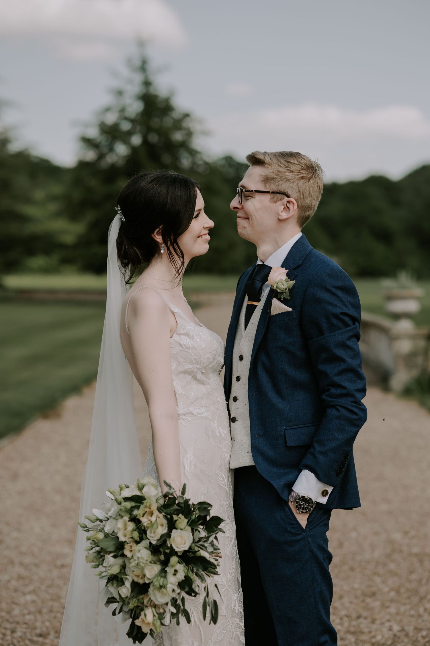 Newlywed couple shares intimate wedding portraits in an outdoor setting with natural greenery and a white floral bouquet.