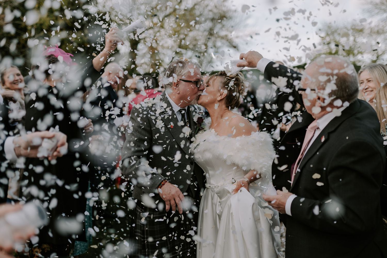 Wedding couple and guests celebrate with confetti and bubbles during outdoor ceremony in black and white.
