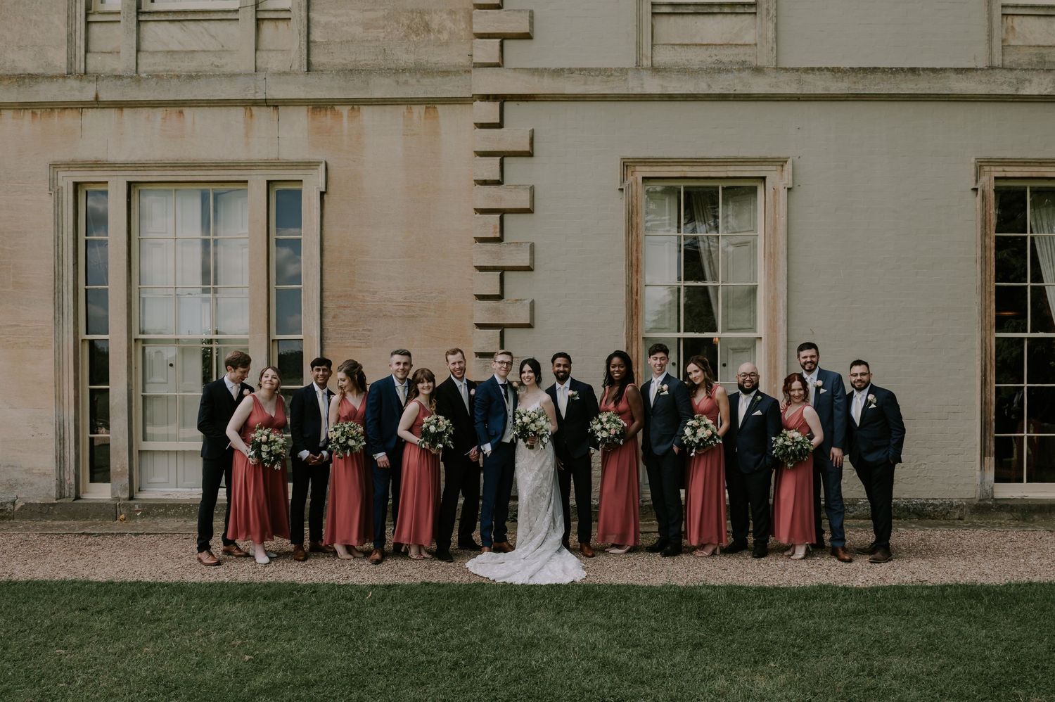 Wedding party stands in line against elegant stone building façade with tall windows and columns in classic pose.