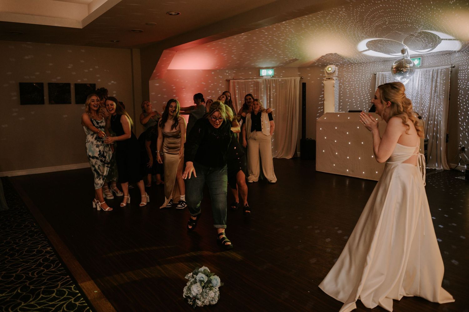 Bride throws bouquet as guest runs to catch it in sunlit venue, Melton Mowbray wedding.