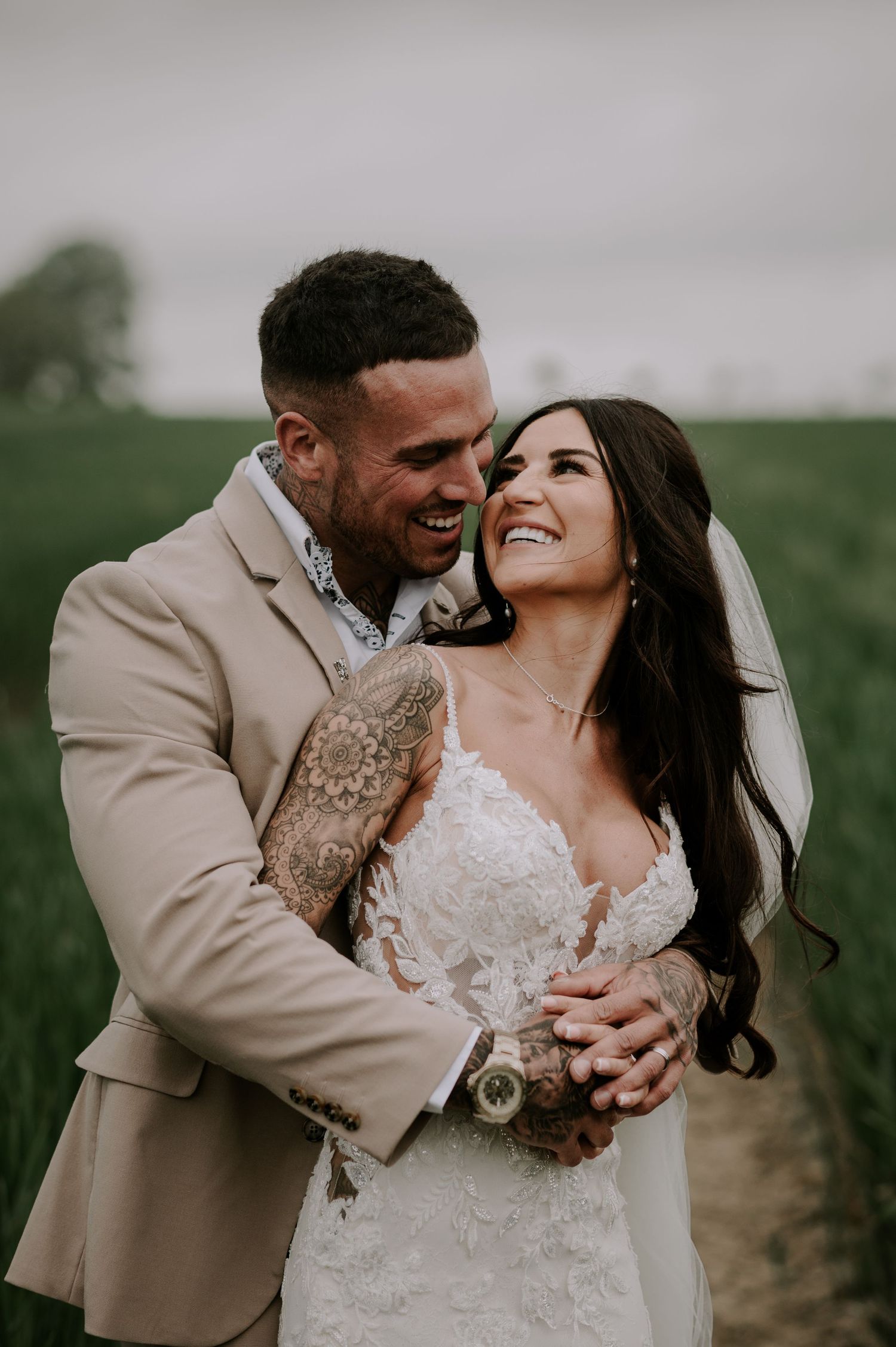 A joyful newlywed couple embraces and laughs together in a green field on their wedding day.