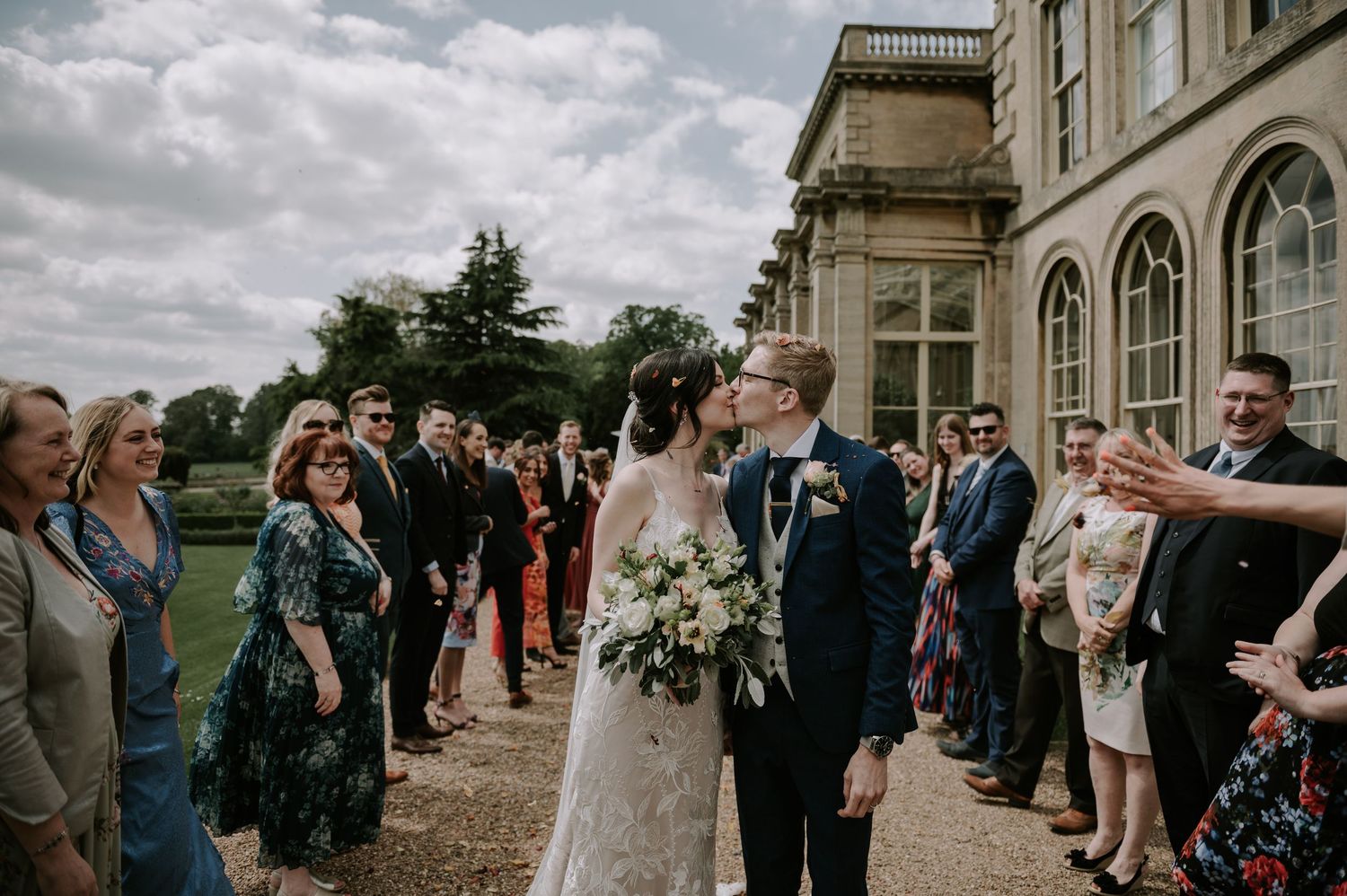 Wedding guests gather outside a grand historic building to celebrate a special moment between newlyweds.
