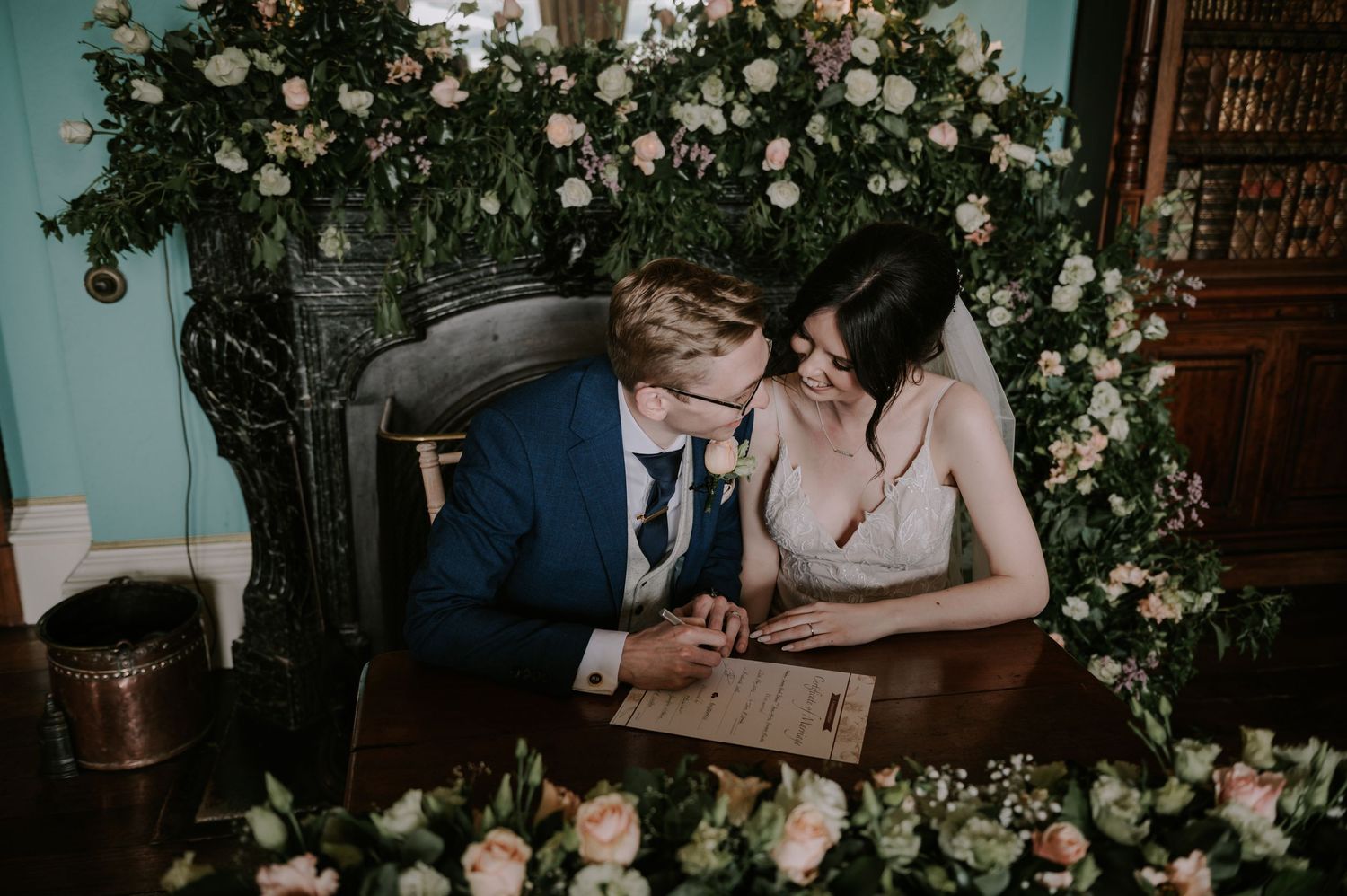 Couple signing documents at an elegant wedding ceremony venue decorated with white floral arrangements.