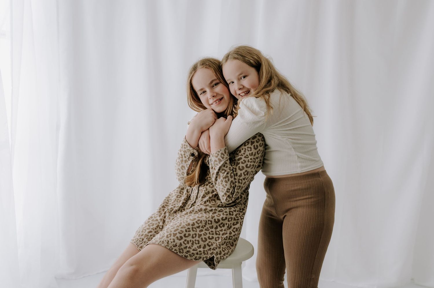 Sisters embracing and smiling, studio in bright neutral tones, Melton Mowbray.