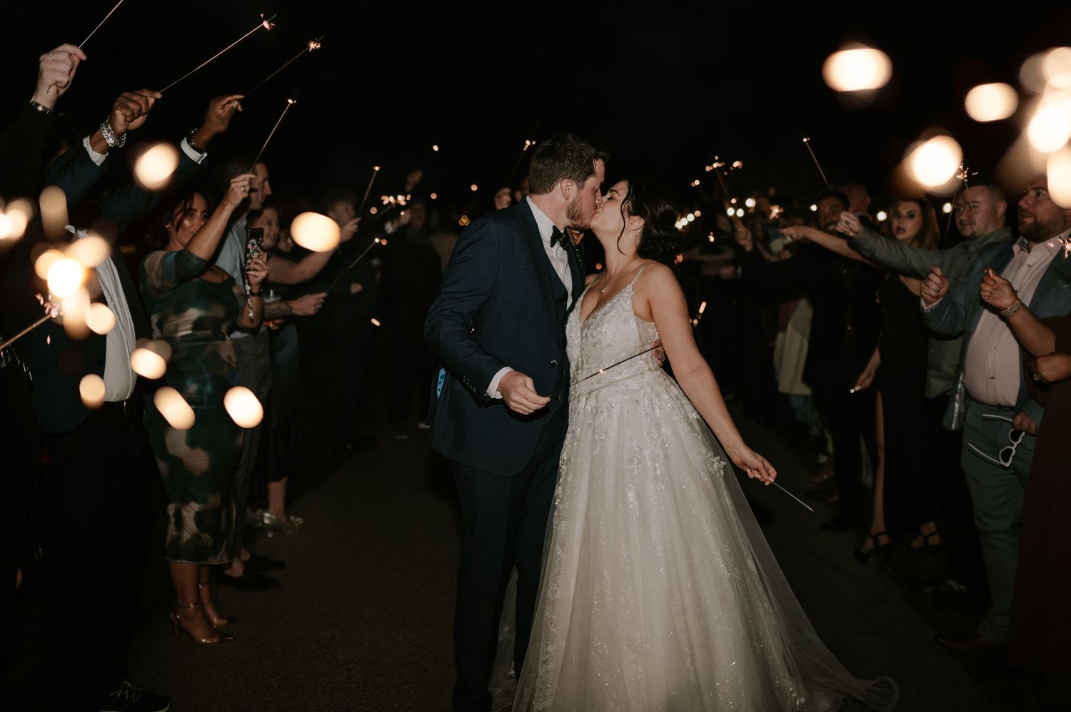 People dance together in a dimly lit room with glowing lights during what appears to be a wedding reception celebration.