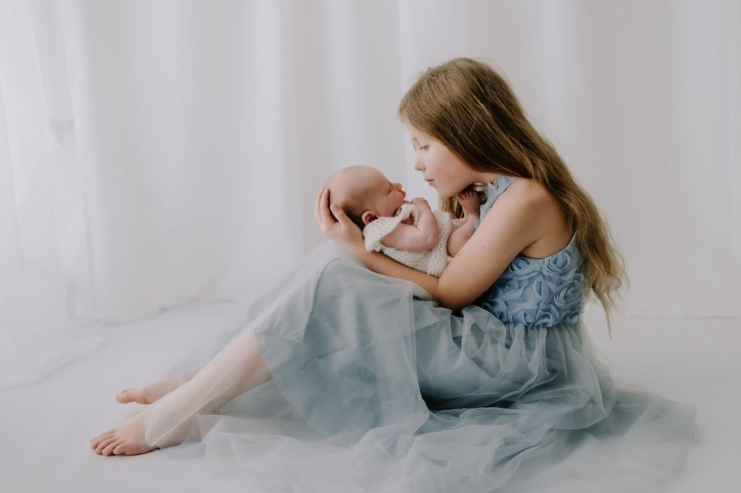 Girl in a blue dress cradling her newborn brother in a studio – Melton Mowbray family and newborn photoshoot.