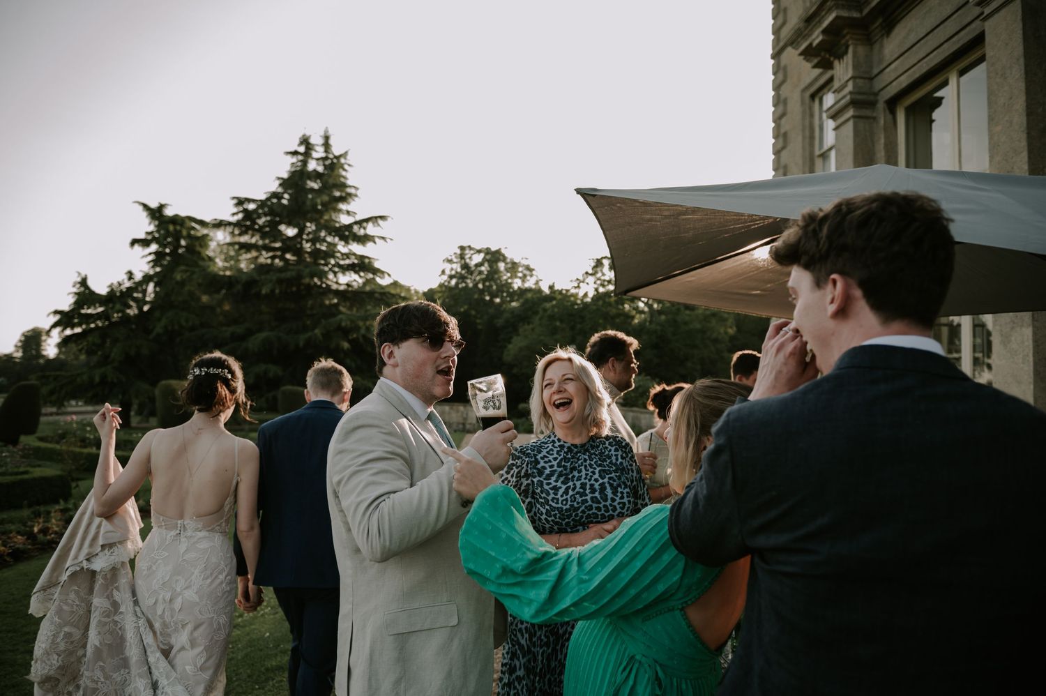 Wedding guests socialize and laugh together during an outdoor reception at dusk.