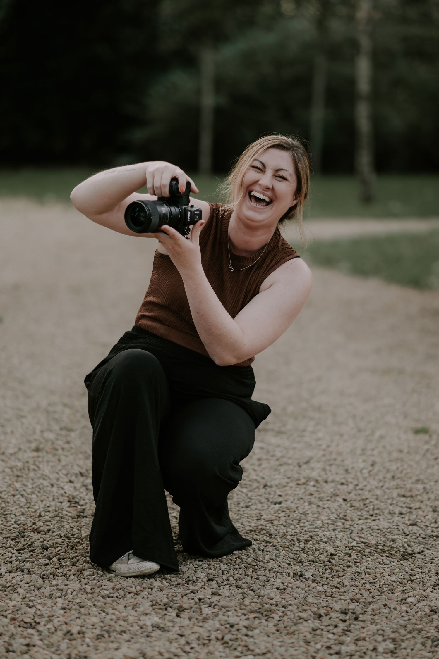 A photographer in dark clothing crouches low to capture shots from different creative angles outdoors.