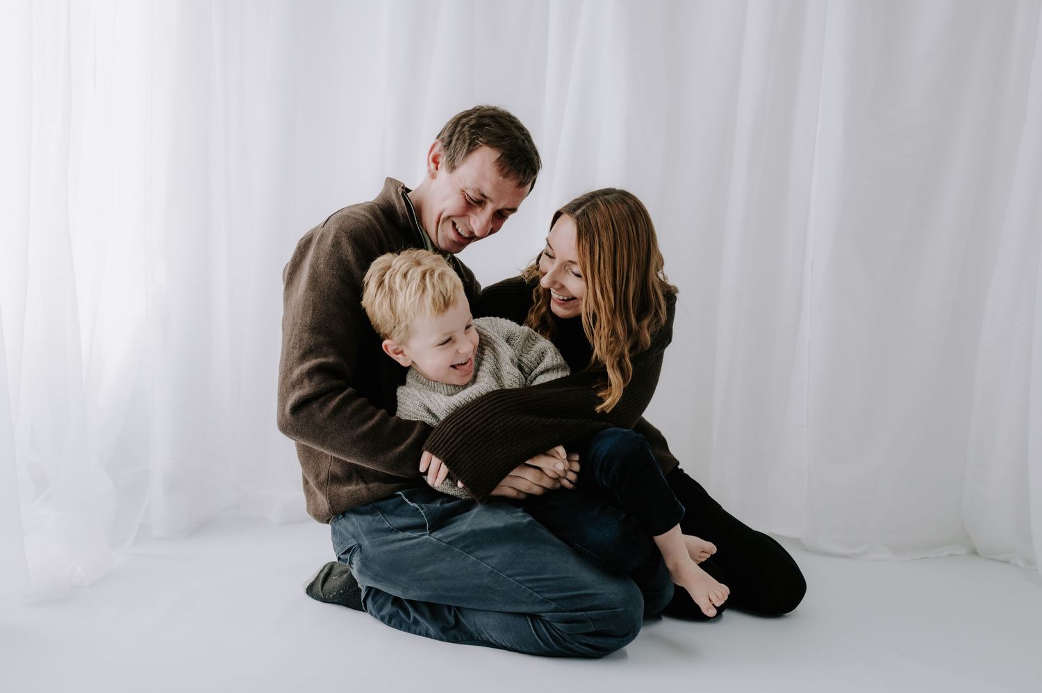 Family in dark clothing playing tickles on studio floor, family session, Melton Mowbray.