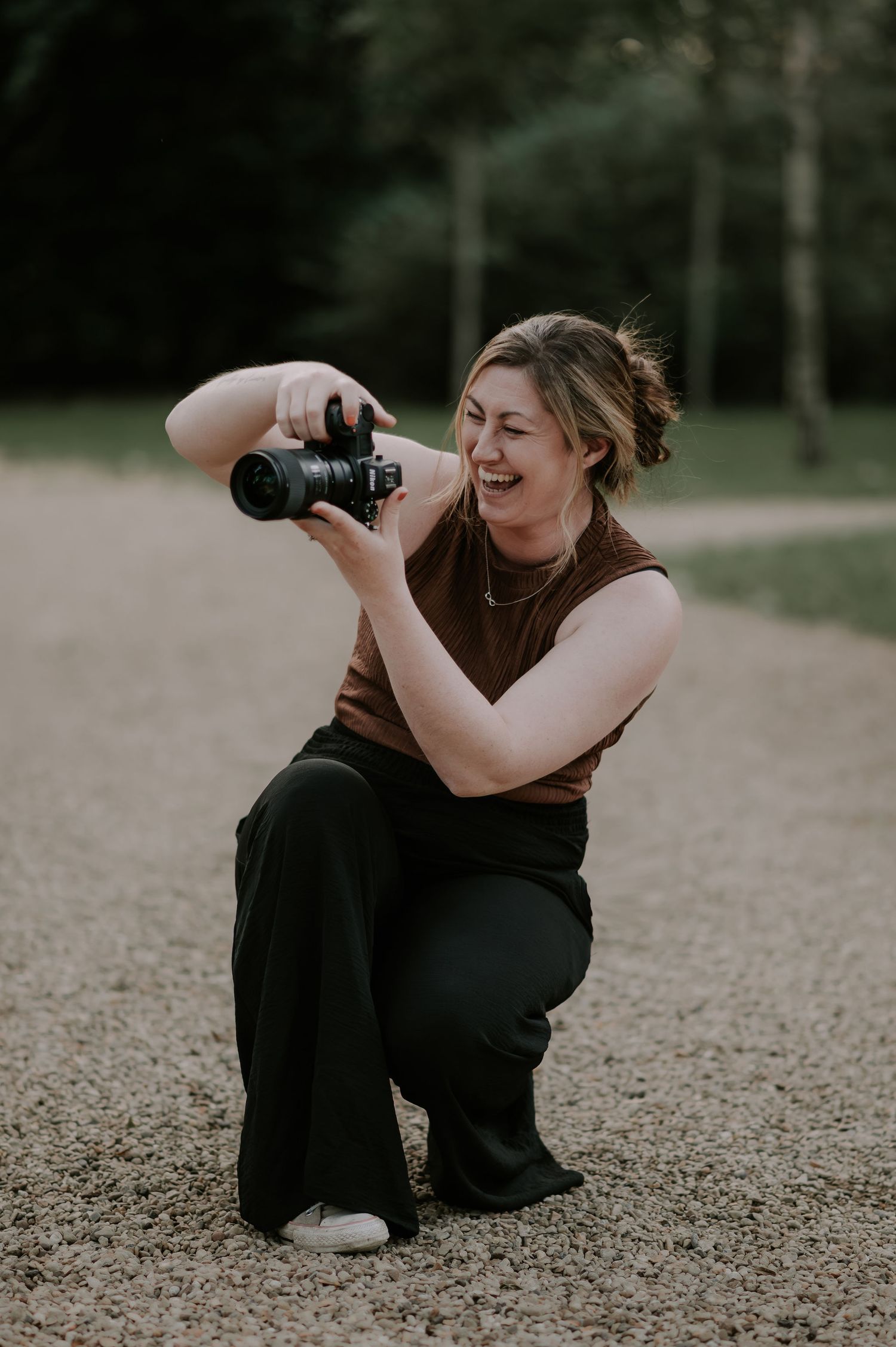 A photographer in black clothing lies on the ground taking creative shots from different angles outdoors.