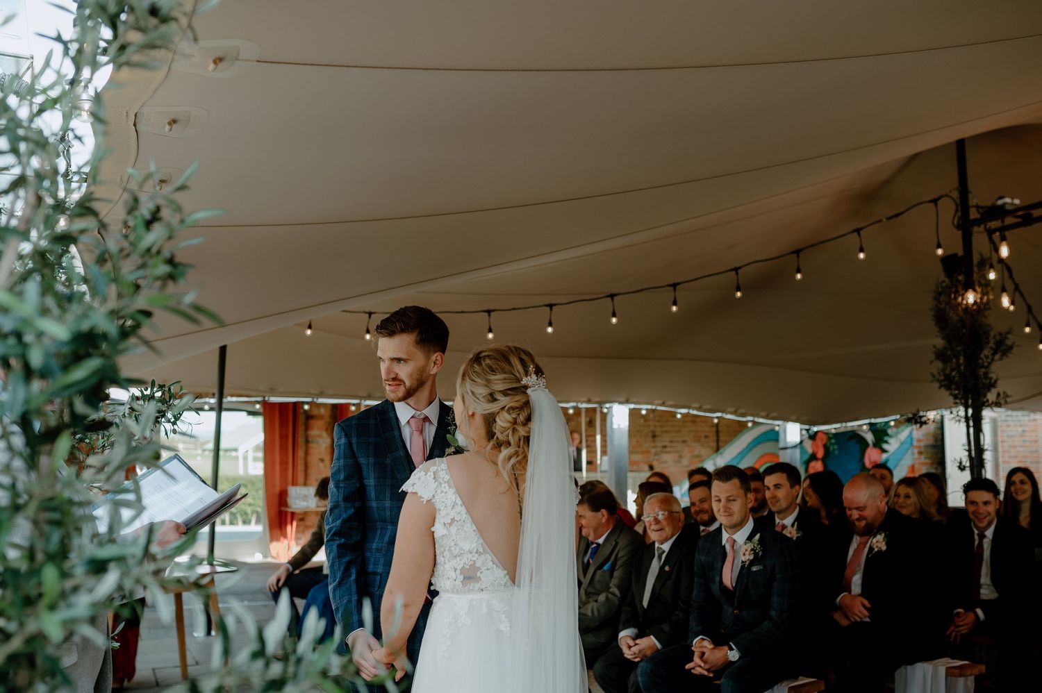 A couple shares their first dance under a tent decorated with string lights at an outdoor wedding celebration.