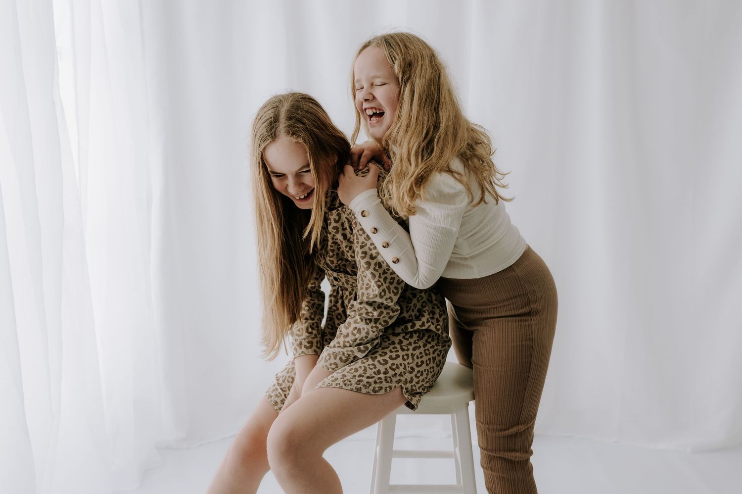 Joyful sisters laughing and embracing in bright white studio, Melton Mowbray.