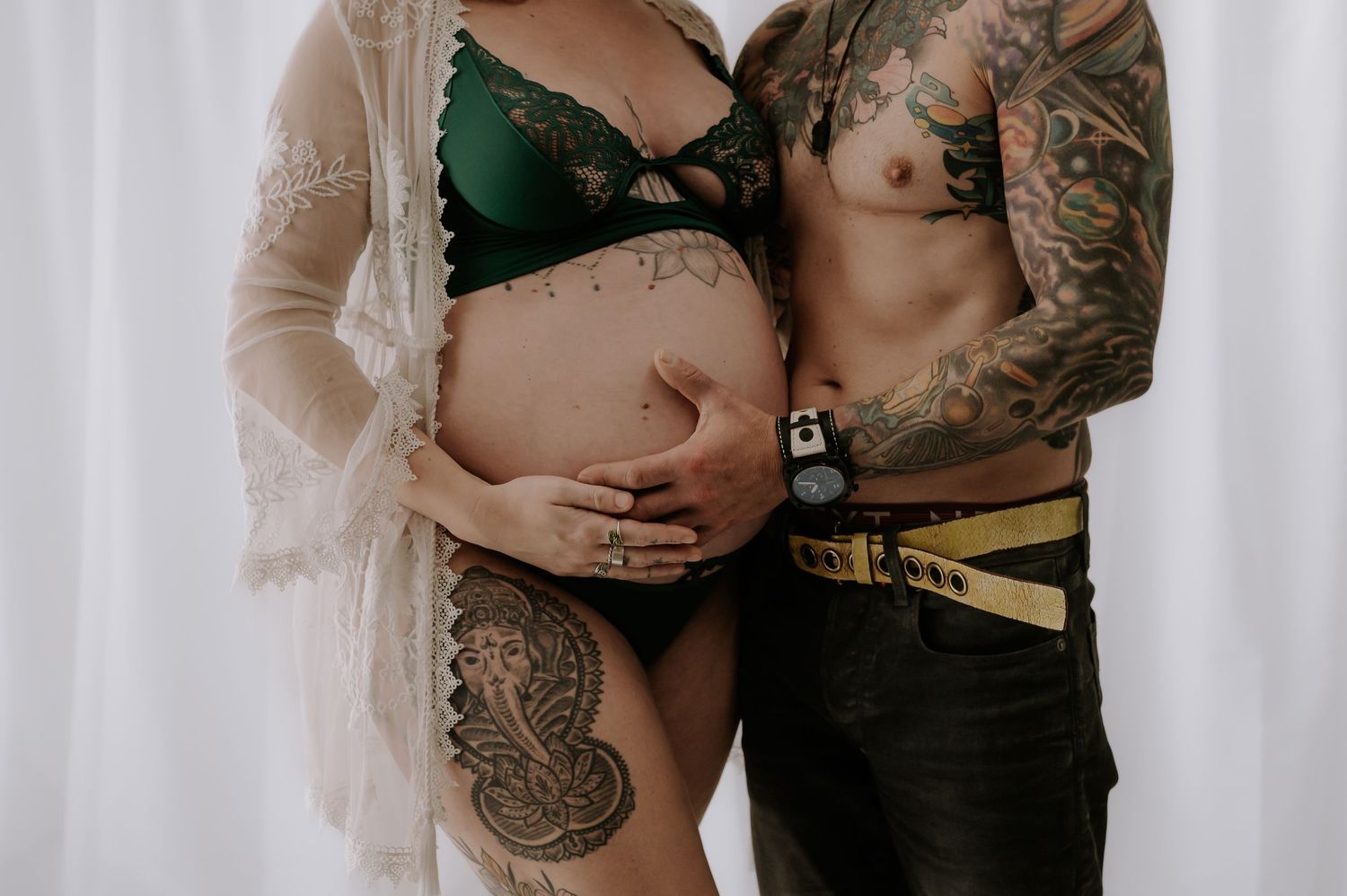 Intimate maternity couple pose, tattoos visible, woman in white lace gown, studio, Melton Mowbray.