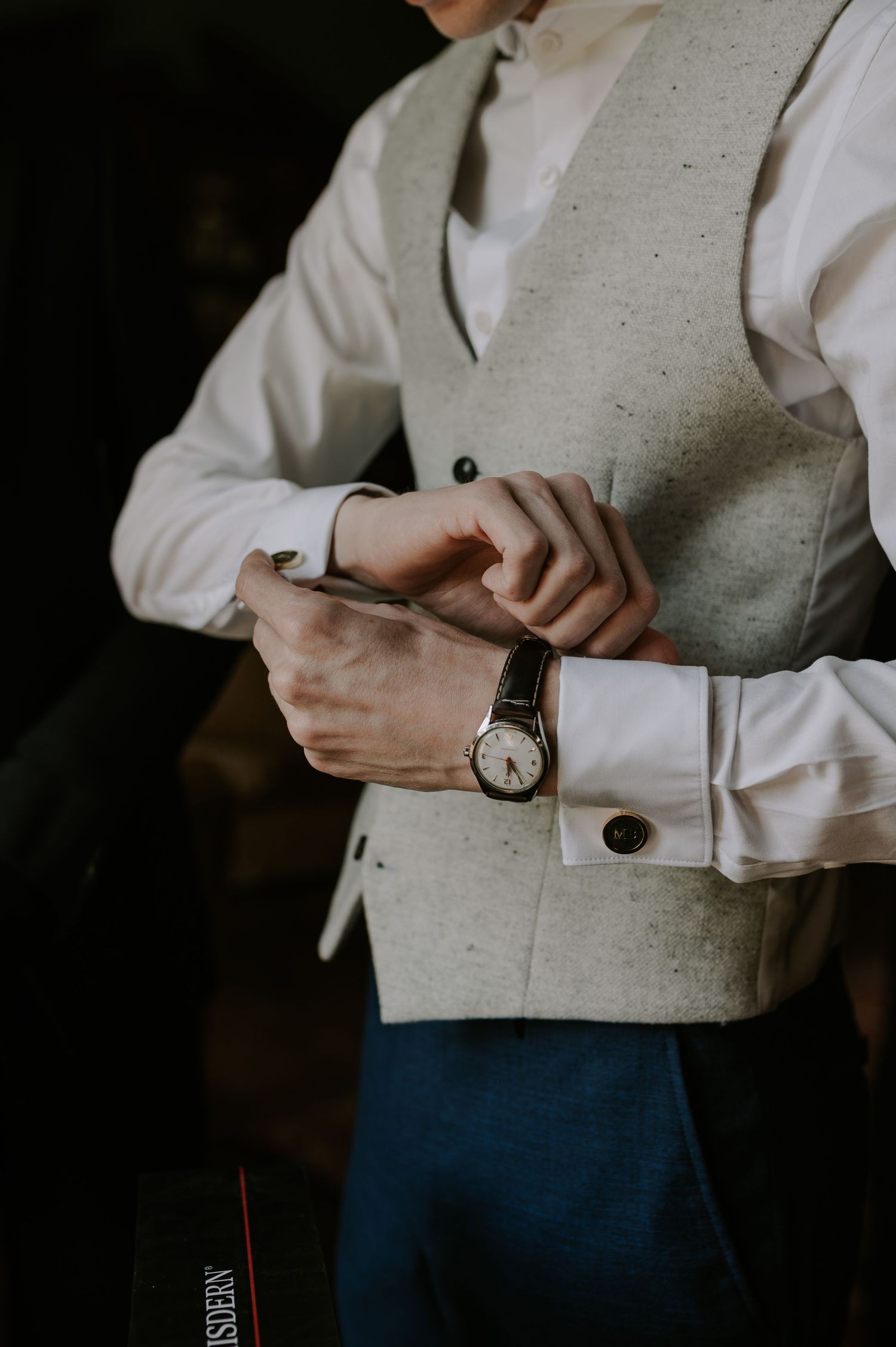 Close-up view of hands adjusting sleeves and wristwatch with a light gray vest and white shirt.