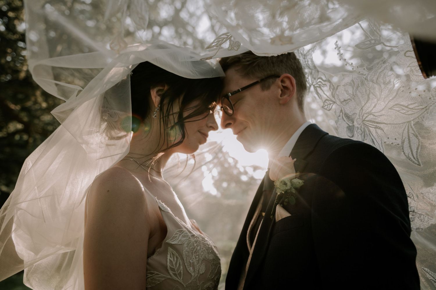 A romantic wedding moment captured under a veil with soft sunlight creating an ethereal glow.