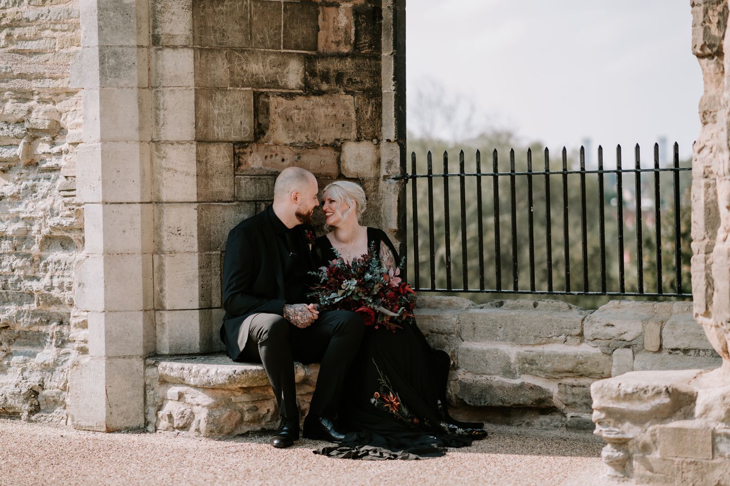 A couple shares an intimate moment while sitting on stone steps against an old stone wall.