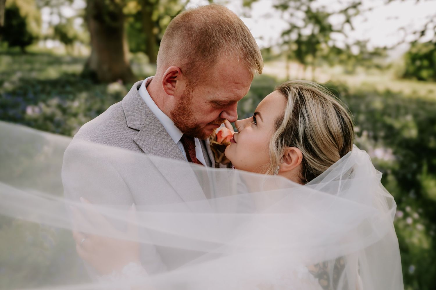 The couple shares a romantic kiss enveloped in flowing white wedding veil during their outdoor ceremony.