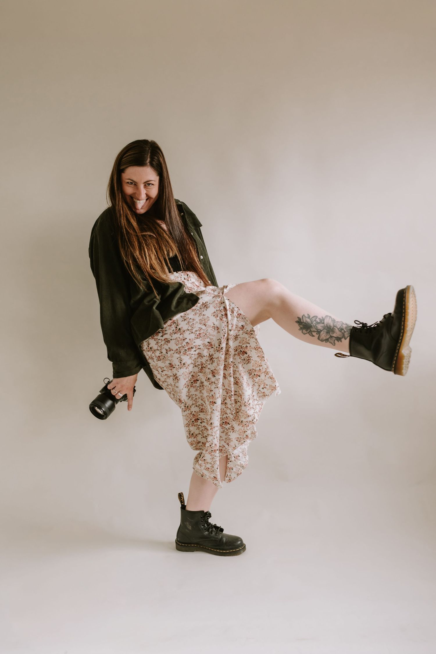 Someone wearing a black sweater and floral skirt kicks up one leg while wearing combat boots against a neutral background.