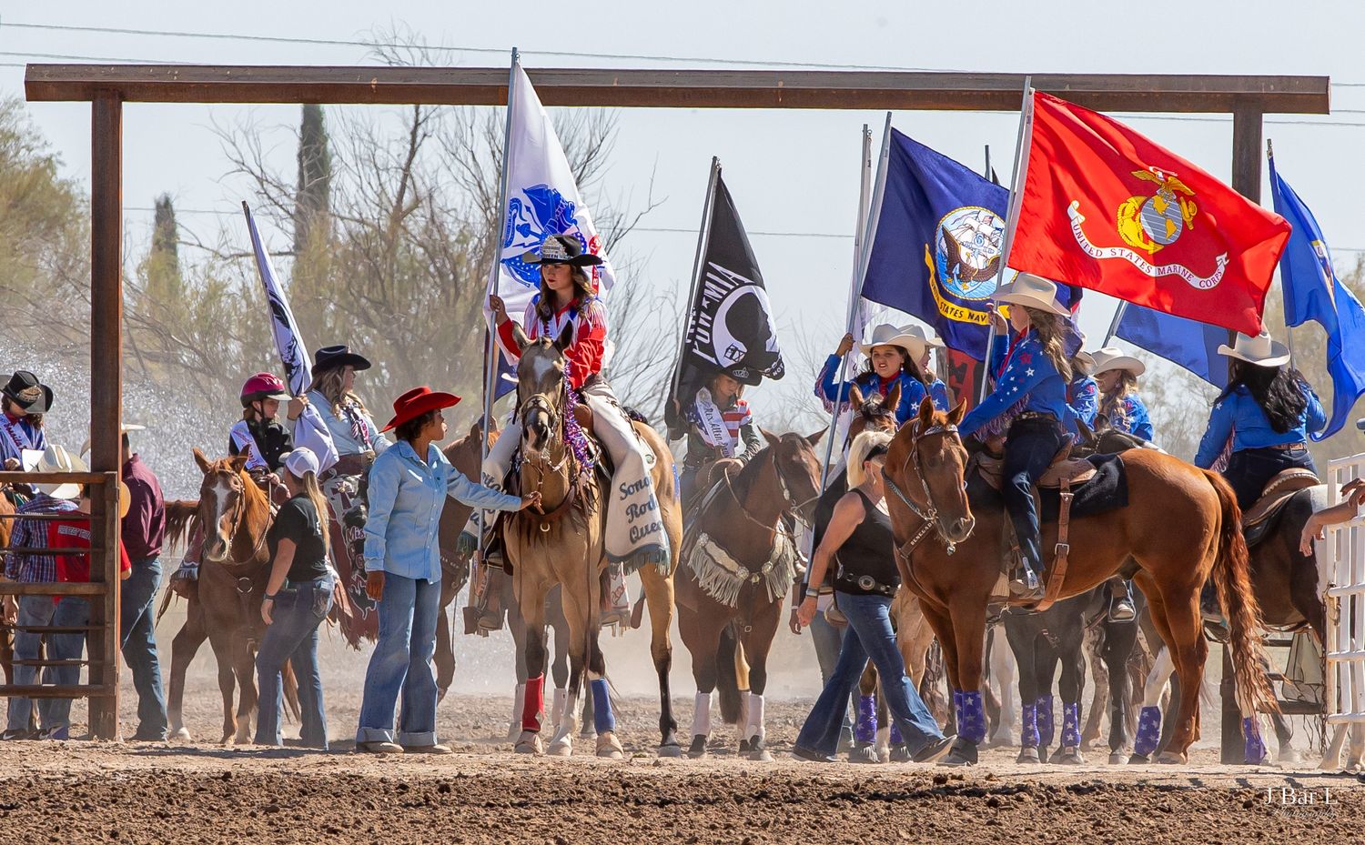 Horseback riders carrying American and military flags during a colorful rodeo opening ceremony.