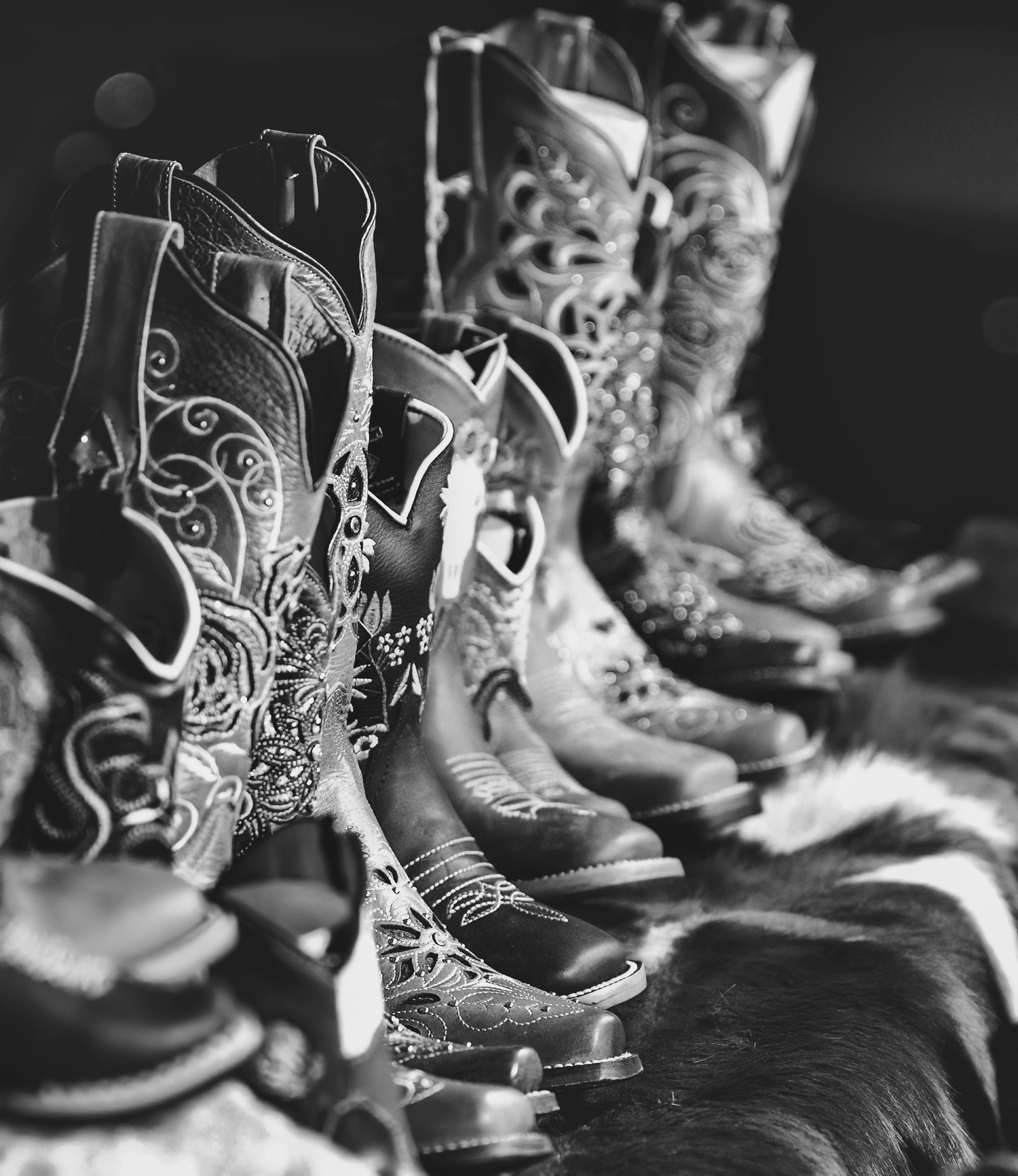 A collection of ornate cowboy boots lined up in a row, showcasing intricate Western designs in black and white.