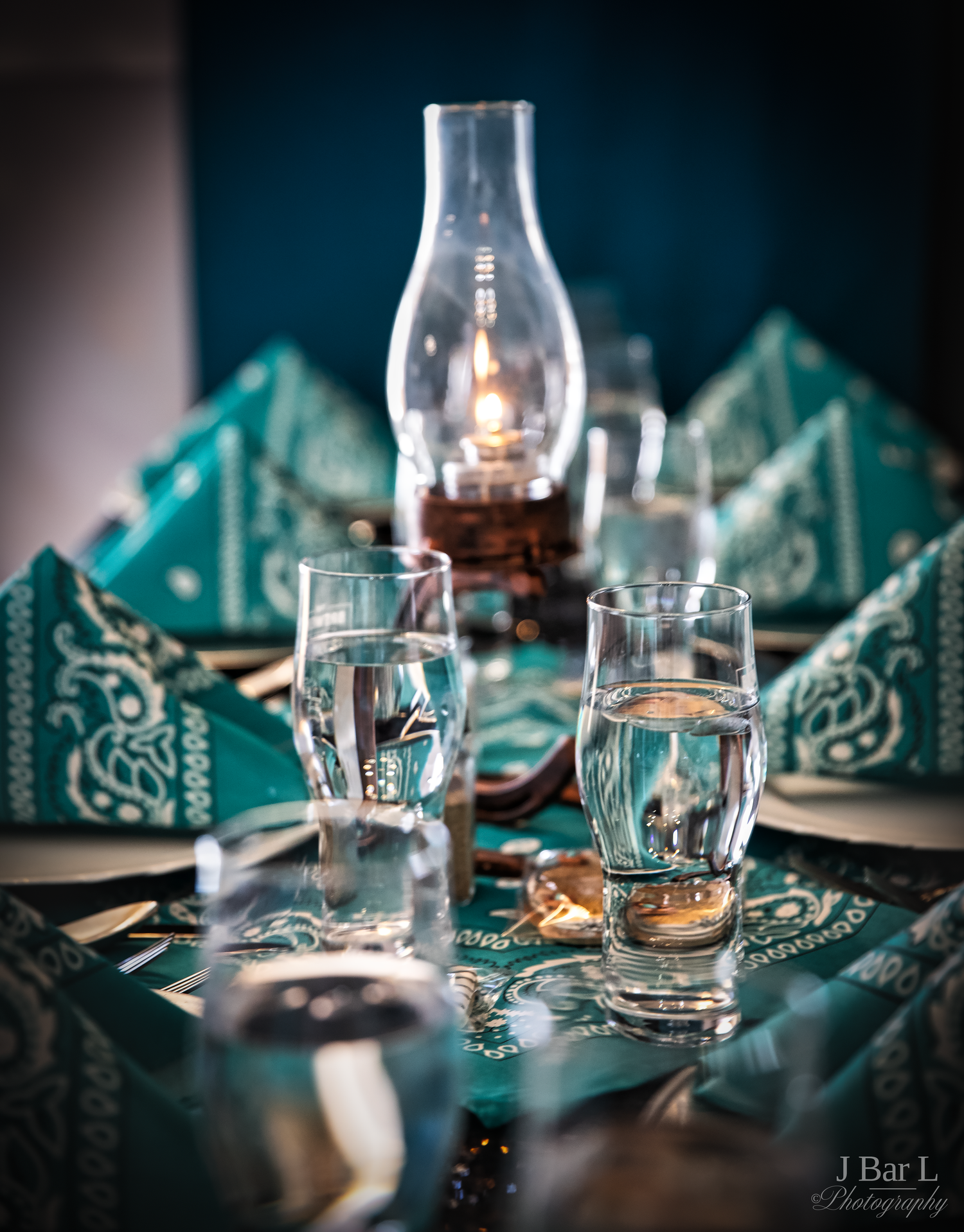 Elegant table setting with teal napkins, water glasses, and a vintage oil lamp centerpiece.