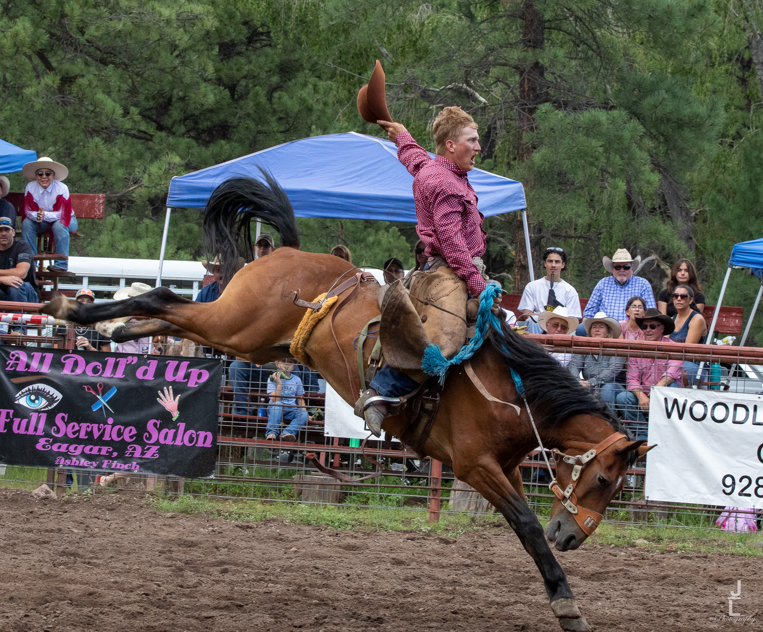 Female rodeo rider in pink shirt on bucking bronco during outdoor rodeo competition.