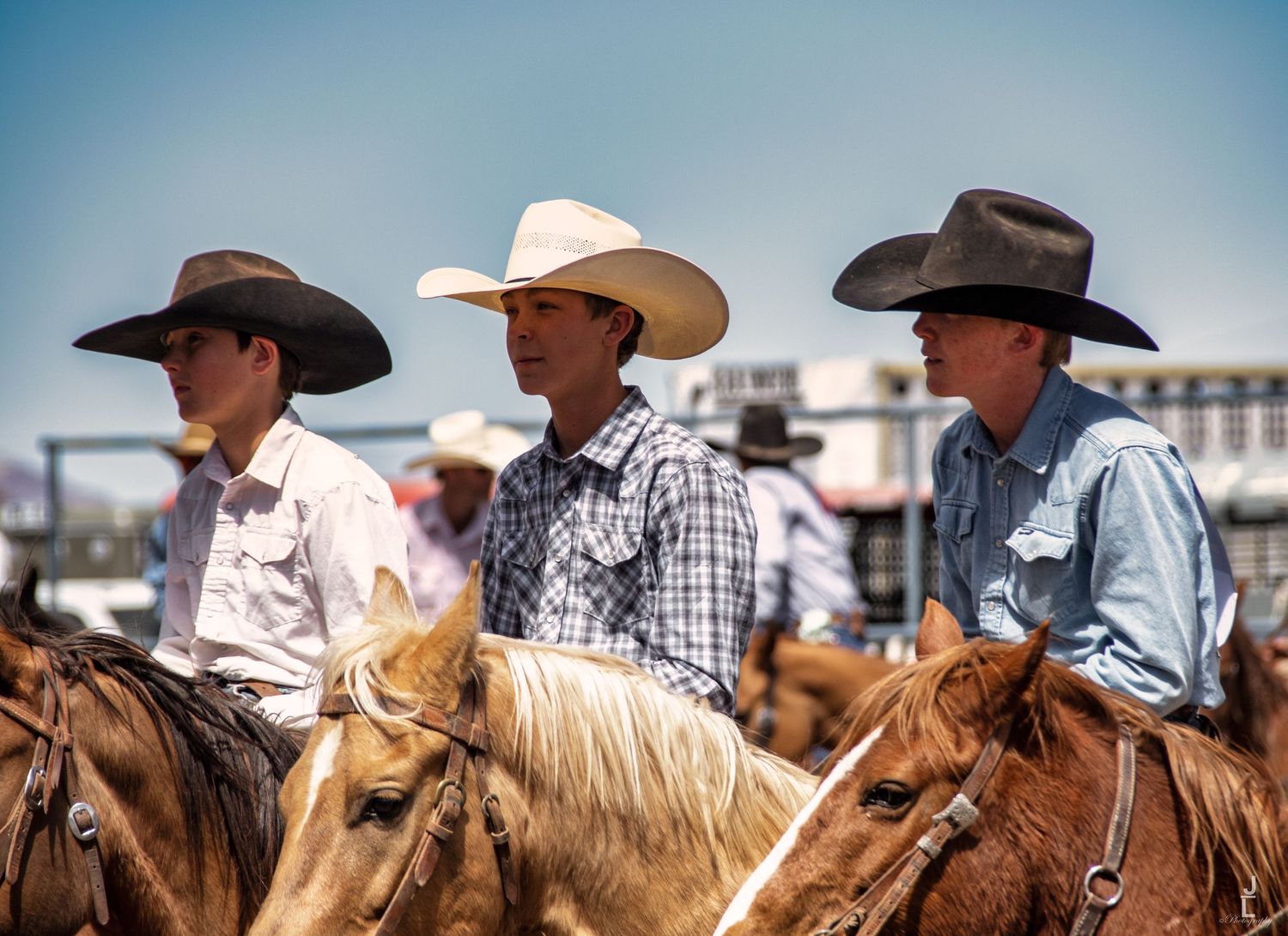 Three young male cowboys on horseback wearing cowboy hats at a sunny outdoor rodeo event.