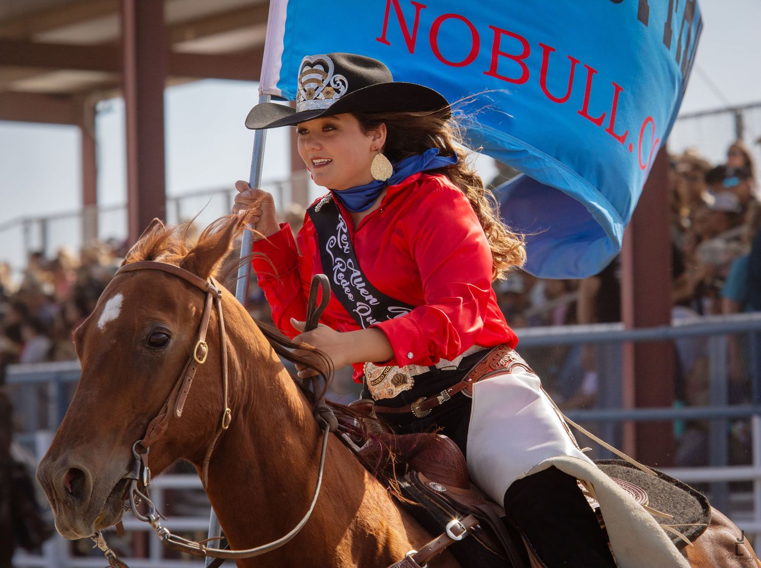 A rodeo queen on horseback carries a NoBull sponsor banner during a rodeo opening ceremony.