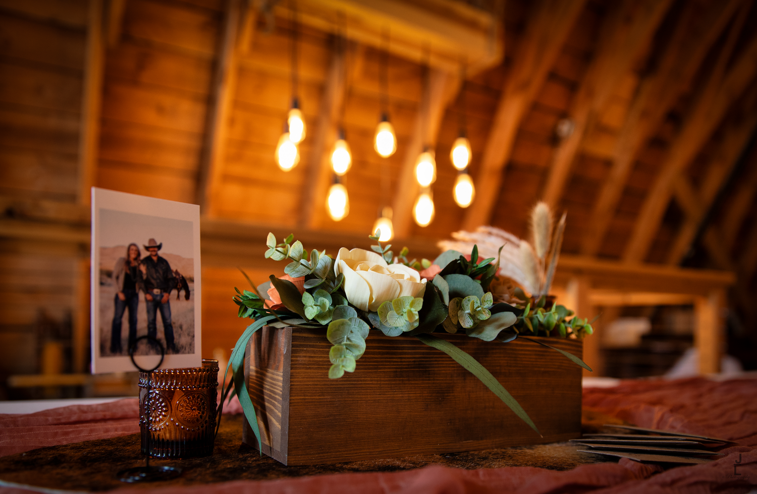 Rustic wooden box centerpiece with white flowers and photo in warmly lit barn.