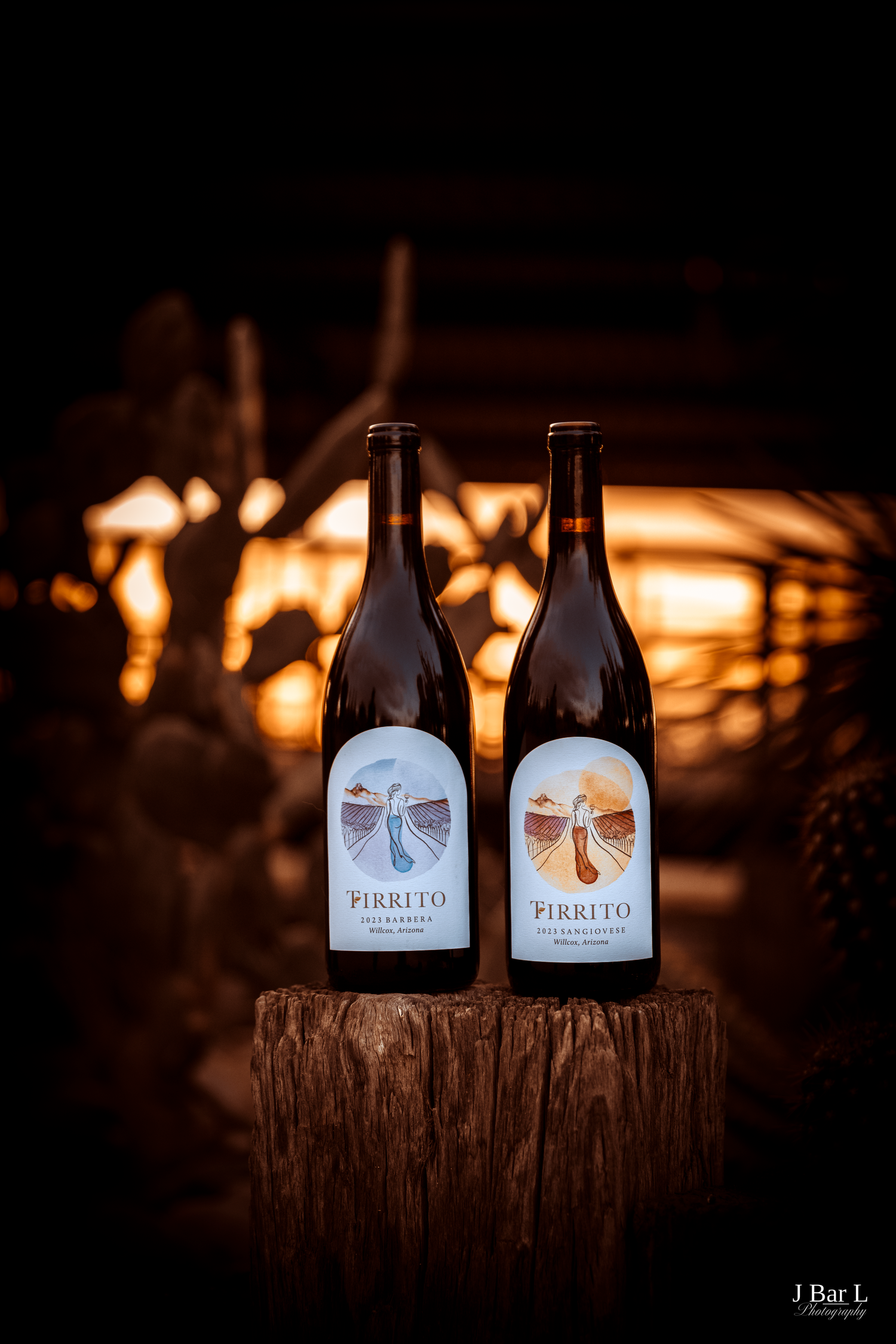 Two bottles of Pirrito wine displayed on a wooden stump with warm bokeh lights in the background.