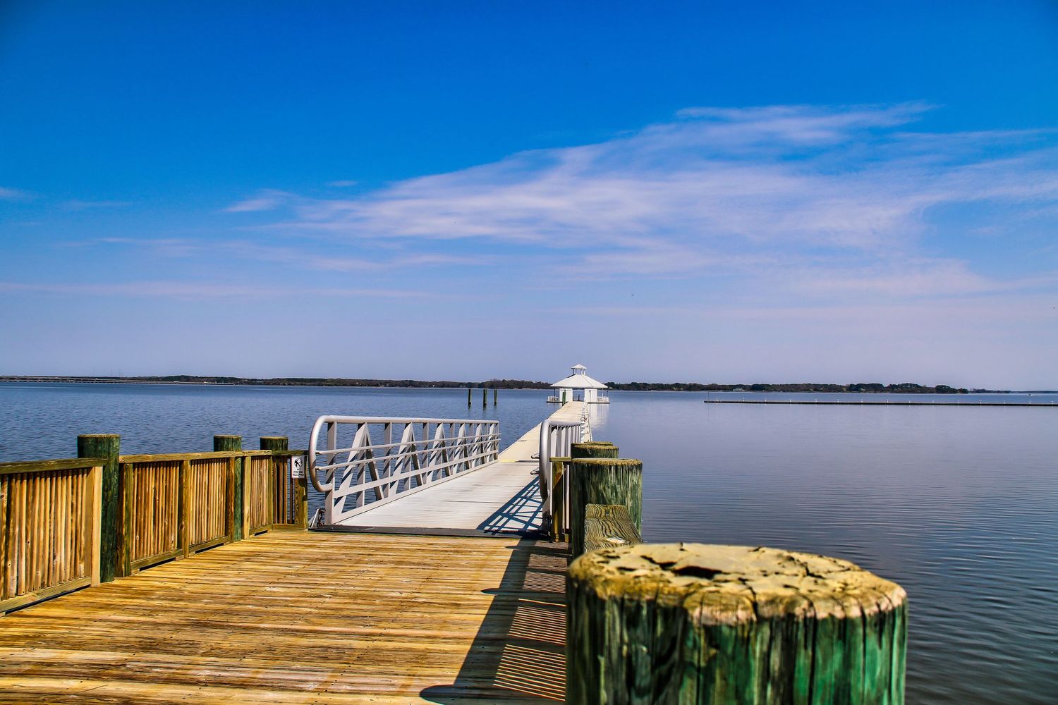 A serene wooden dock extends over calm blue waters under a bright sky at a peaceful coastal marina.