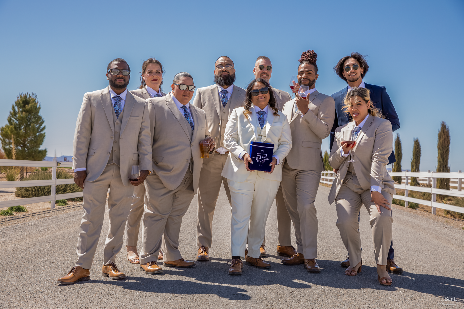 Group of nine people in tan and navy suits pose together outdoors on a sunny day.